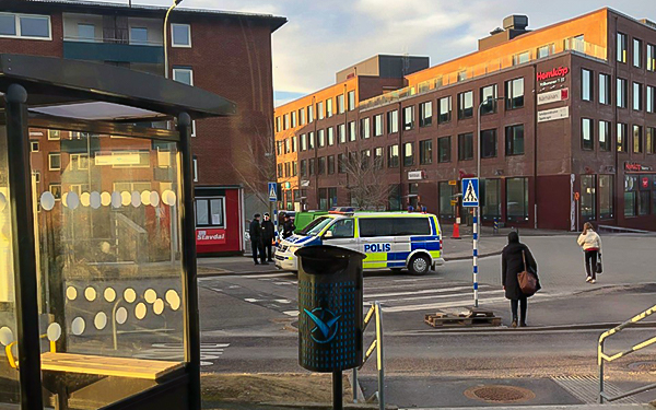 En gata med en polisbil. Två poliser står bredvid med en man. I bakgrunden syns byggnader