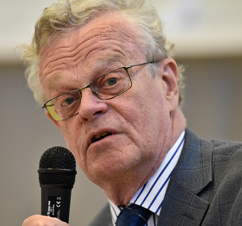 Bild på Björn Eriksson. Håller i en mikrofon. Äldre man i vitt hår och har på sig smala glasögon